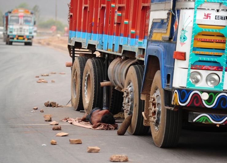 Truck driver resting under truck in India